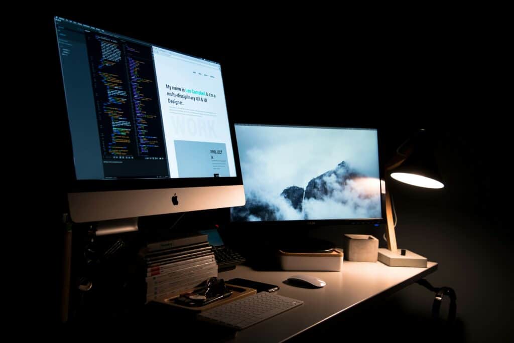 iMac & desktop computer placed on a professional working desk with a lamp in a dark room